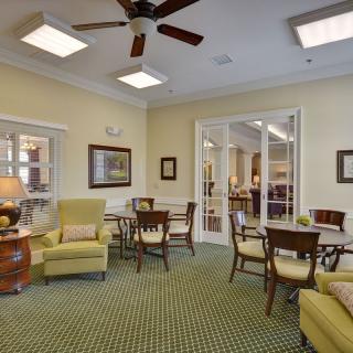 A cozy and well-furnished living room with chairs, tables, and a ceiling fan.
