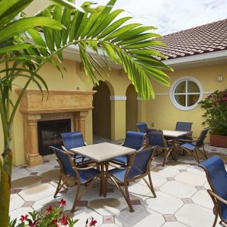 An inviting patio features tables and chairs under the shade of a palm tree, set against yellow walls with a fireplace.