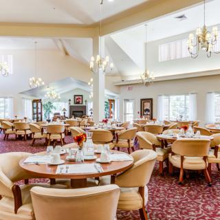 A spacious and elegantly decorated dining area with multiple tables and chairs, featuring chandeliers and a warm ambiance.