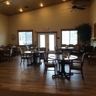 A cozy dining area with wooden floors and ample natural light, featuring tables and chairs arranged for a relaxed setting.