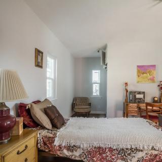 A cozy bedroom with a bed, side table, lamp, and a desk.