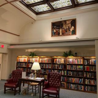 A cozy library reading nook with two leather chairs, a small table, and shelves filled with books.