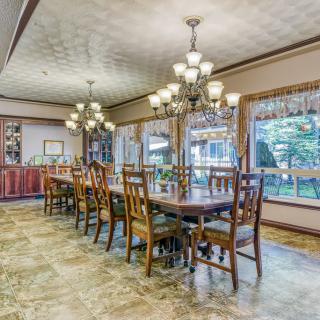 A spacious dining room with a long table and wooden chairs, illuminated by elegant chandeliers.