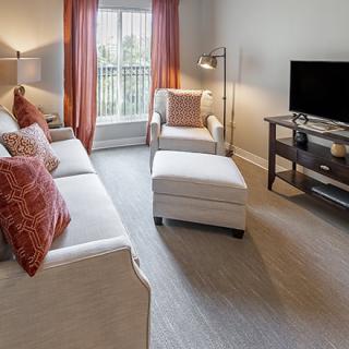 A cozy living room with a sofa, armchair, and ottoman arranged around a television, featuring warm curtains and soft lighting.