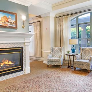 A cozy living room with a fireplace, two chairs, and a large window letting in natural light.