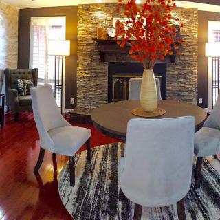A modern dining room with elegant furnishings, featuring a stone fireplace, round table, and decorative vase centerpiece.