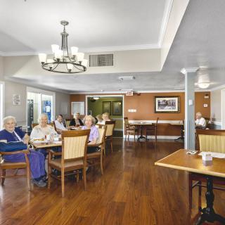 A dining area with seniors seated at tables, featuring a wooden floor and chandelier.