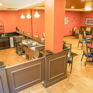 A cozy restaurant interior featuring a bar counter, wooden flooring, and neatly arranged dining tables and chairs.