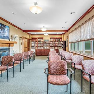 A spacious waiting room with chairs arranged in rows, a television mounted above a fireplace, and bookshelves along the back wall.