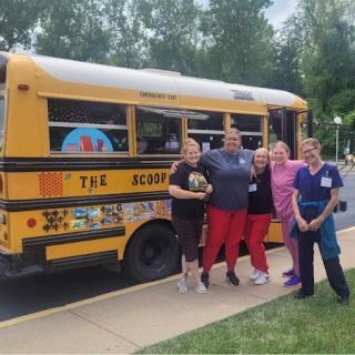 A cheerful group of individuals gathered in front of a colorful school bus, celebrating a community event.