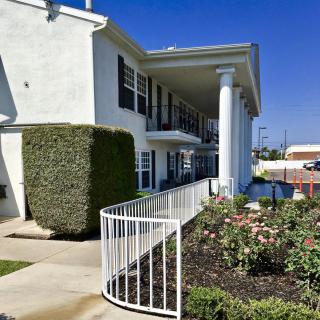 A sunny exterior view of a two-story apartment building with a garden and walkway.