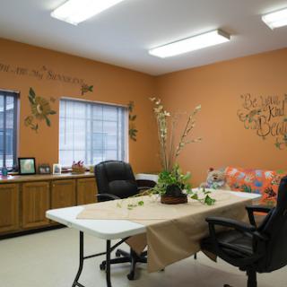 A cozy office space with orange walls and a simple setup, featuring decorative plants and comfortable seating.