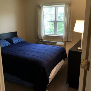 A cozy bedroom with a bed covered in blue bedding, a lamp on a bedside table, and a window with curtains.