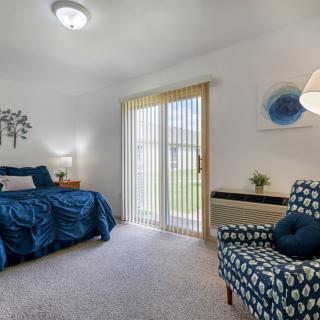 A cozy bedroom with blue accents and natural light coming through vertical blinds.