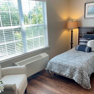 A cozy bedroom with a single bed, a chair by the window, and a floor lamp.
