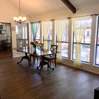 A bright and elegant dining room featuring a wooden table and large windows adorned with sheer curtains.