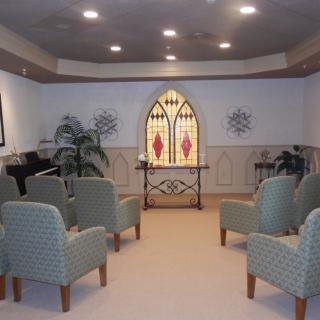 A small chapel with seating, stained glass window, and decorative elements.