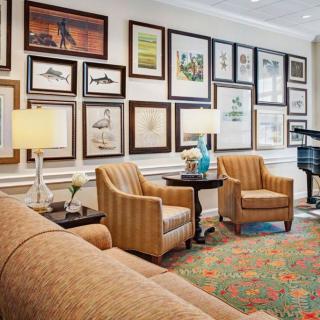 A cozy living room with a gallery wall of various artworks, comfortable seating, and a piano.