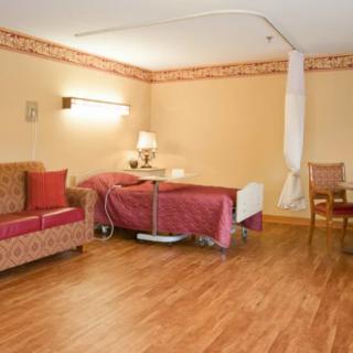A hospital room with a bed, sofa, and chair on a wooden floor.