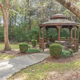 A serene garden with a wooden gazebo surrounded by trees and greenery.