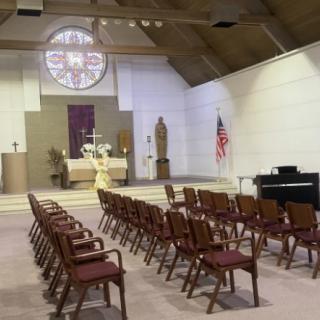The interior of a church featuring rows of pews, an altar with religious symbols, and a stained glass window in the background.