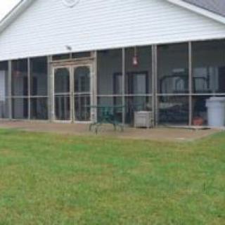 A suburban house with a screened porch and a green lawn in the backyard.