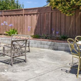 A sunny patio area with outdoor chairs and a table near a wooden fence.