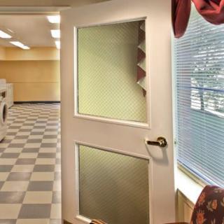 A laundromat interior with a checkered floor and an open door leading to a room with ceiling lights.