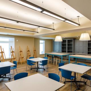 A well-lit art classroom featuring easels, tables, and chairs, creating an inviting space for creativity.