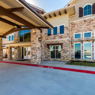 A modern building with a stone facade and large windows, featuring a prominent entrance and driveway.