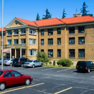 A brick building with a red roof, surrounded by parking and trees on a sunny day.