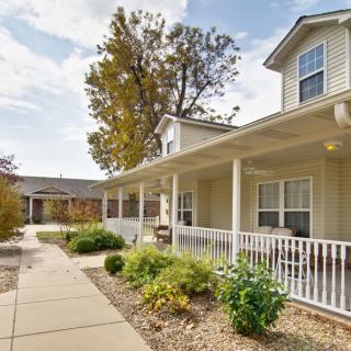 A charming house with a porch, surrounded by a garden and trees under a clear sky.