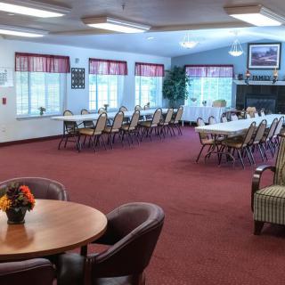 A spacious dining or conference room with multiple tables and chairs, featuring a red carpet and large windows with curtains.