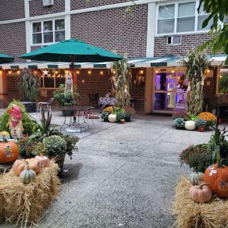 A cozy outdoor space decorated for autumn, featuring pumpkins, hay bales, and festive lighting.