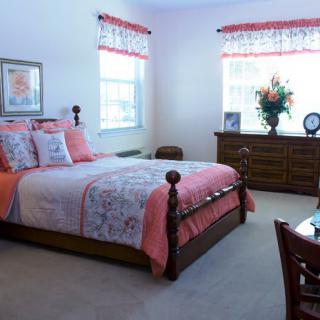 A cozy bedroom with a wooden bed frame and floral bedding, complemented by a large dresser and decorative accents.