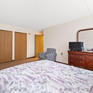 A bedroom with a bed, dresser, television, and patterned chair.