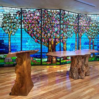 A beautifully designed interior featuring a stained glass wall with tree motifs and natural wood tables.