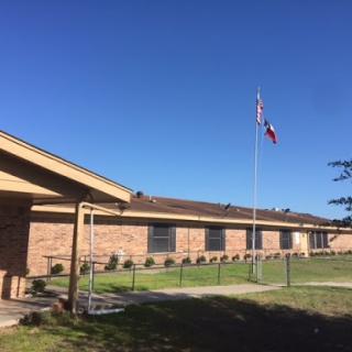 A school building featuring a Texas flag under a clear blue sky.