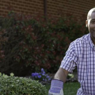 A man in a checkered shirt and gloves is tending to his garden.