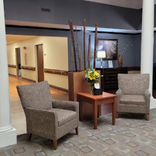 A cozy waiting area featuring two plush chairs, a wooden table with a flower arrangement, and soft lighting.