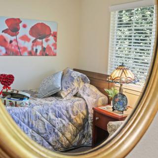 A cozy bedroom interior reflected in a mirror, featuring a bed, decorative lamp, and a floral painting.