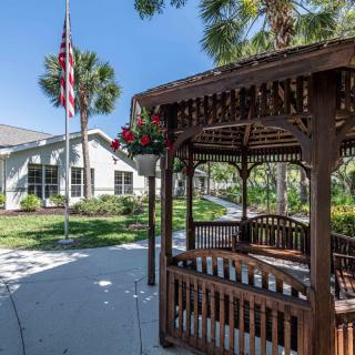 A wooden gazebo in a landscaped garden with an American flag and a nearby building.