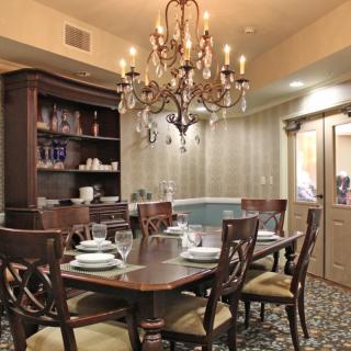 A traditional dining room featuring a wooden table set with place settings, surrounded by chairs and illuminated by an elegant chandelier.