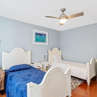 A cozy bedroom with twin beds, blue bedding, and a ceiling fan.