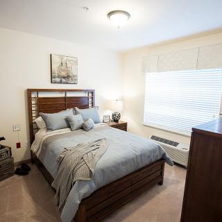 A cozy and well-decorated bedroom with a neatly made bed, wooden furniture, and ample natural light.