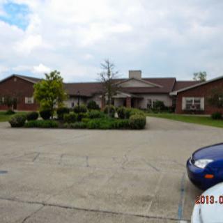 A view of a spacious brick building surrounded by well-maintained landscaping and a parking area.
