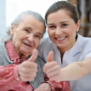 A smiling elderly woman and her caregiver giving a thumbs-up to the camera.