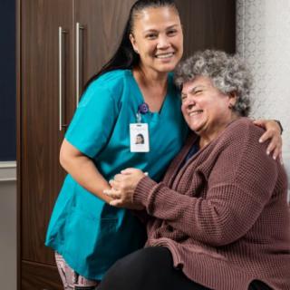 A caregiver and an elderly person share a warm, supportive moment.