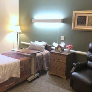 A cozy bedroom with a hospital bed, nightstand, and comfortable chair.