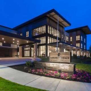 A modern building illuminated at night with a well-lit entrance and landscaped surroundings.